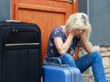Frau sitzt weinend vor Tür mit gepackten Koffern