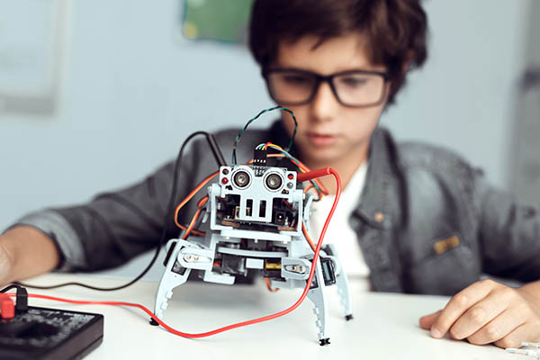 Ein Schüler schaut seinen selbst gebastelten Roboter an, Foto: stock.adobe.com