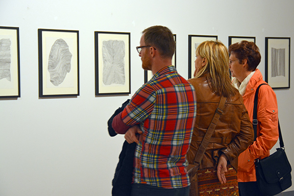 Drei Besucher betrachten in der Ausstellung "Land in Sicht" im Schloss Güstrow Grafiken von Margret Middell.
